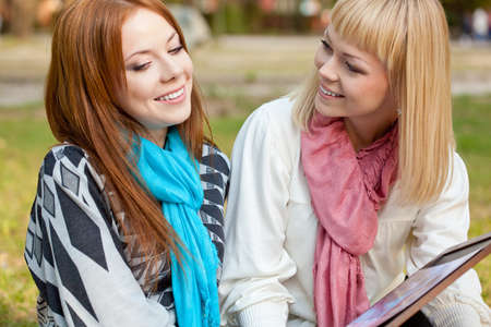 two beautiful sisters with photo album sitting in the summer parkの写真素材