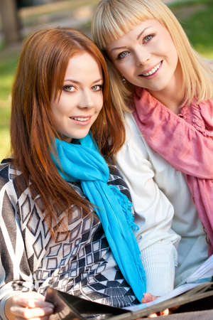 two sisters with photo album sitting in the summer park and looking at cameraの写真素材
