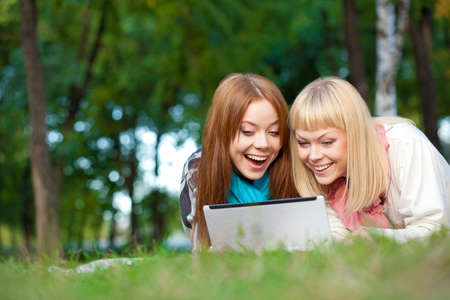two laughing sisters with laptop laying in the summer parkの写真素材