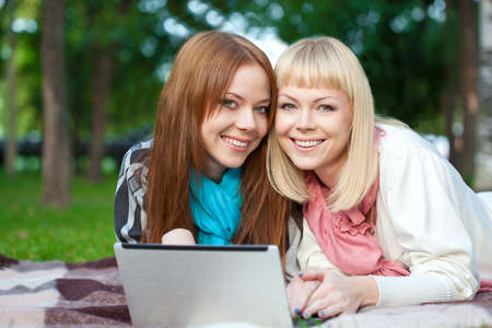 two sisters with laptop laying  in the summer park looking at cameraの写真素材