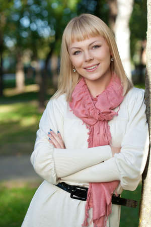 smiling blond woman wearing pink scarf near tree in the summer parkの写真素材