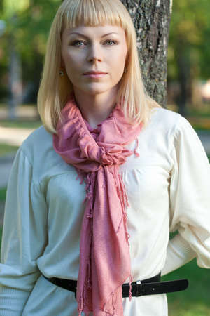blond woman wearing pink scarf near tree in the summer parkの写真素材