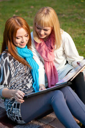 two sisters looking photo album sitting in the summer parkの写真素材