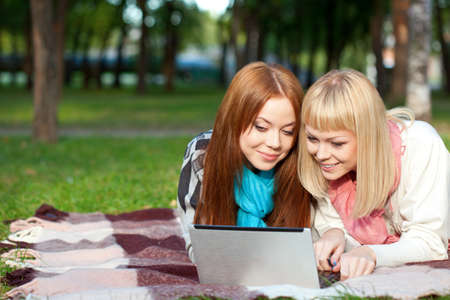 two sisters with laptop laying  in the summer parkの写真素材