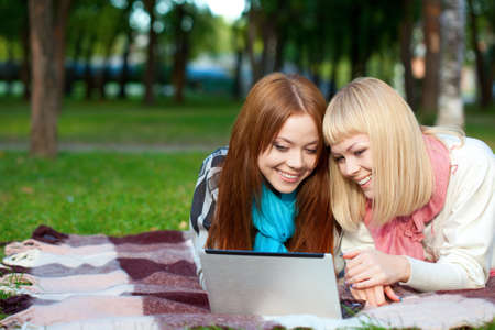 two joyful sisters with laptop laying in the summer parkの写真素材