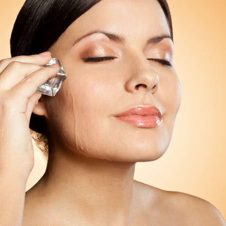 brunette woman holding ice cube on her face, closeup portraitの写真素材