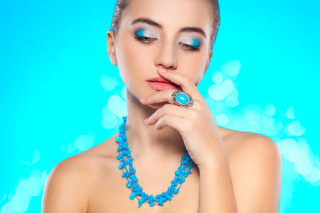 brunette woman looking down with turquoise necklace and ring on fingerの写真素材