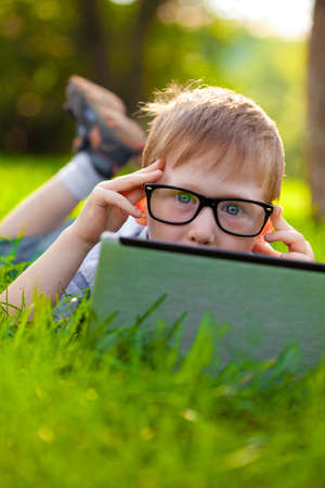 funny little boy looking from behind laptop in the parkの写真素材