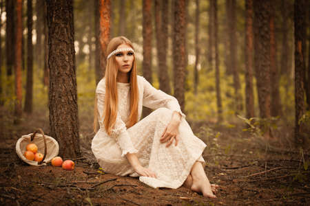 woman sitting on the ground in the woods, next to her is an overturned basket with applesの写真素材