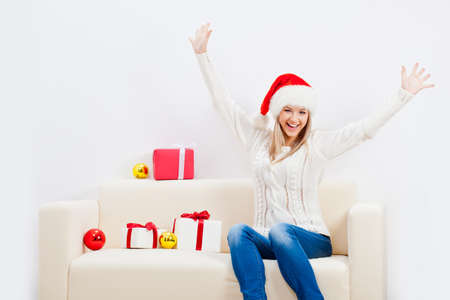 happy woman wearing santa hat sitting on sofa and rising up handsの写真素材