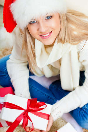 happy blonde woman wearing santa hat sitting on the floor with gifts, top point of view