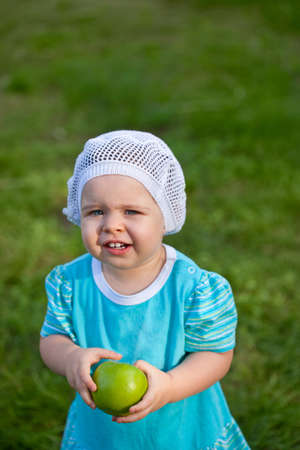cute baby girl wearing blue dress walking in the park and holding green appleの写真素材