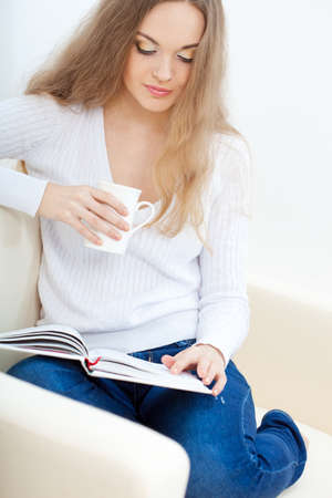 brunette  woman sitting on the sofa with white cup and reading the book