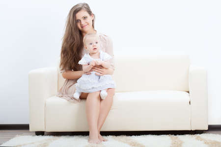 happy beautiful young mother and baby on sofaの写真素材