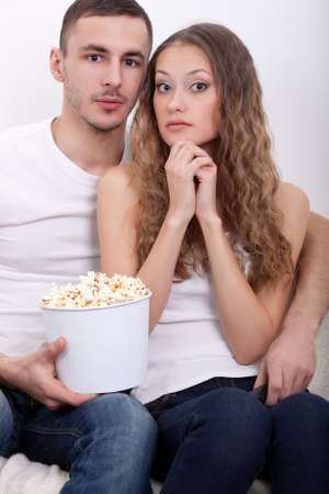young surprised couple sitting on the sofa eating popcorn and watching  tvの写真素材
