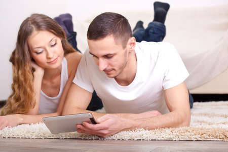 young couple lying on carpet and looking at mini tabletの写真素材