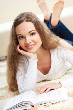 smiling woman lying on carpet with book and looking at cameraの写真素材