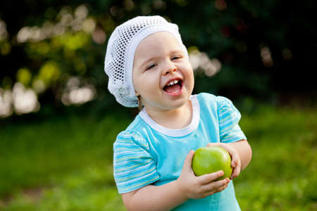cute baby girl  walking in the park and holding green appleの写真素材