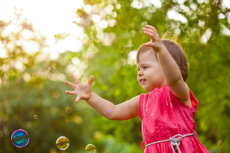 cute little girl wearing pink dress at park with flying bubblesの写真素材