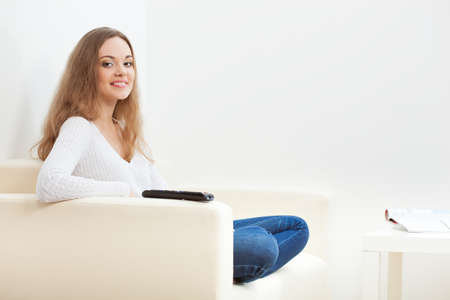 beautiful woman sitting on sofa with remoteの写真素材