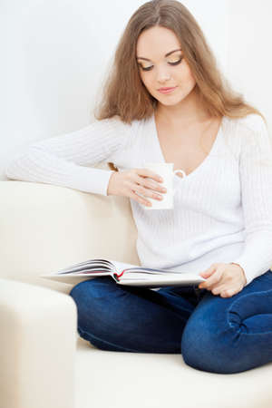 woman sitting on the sofa with white cup and reading the bookの写真素材