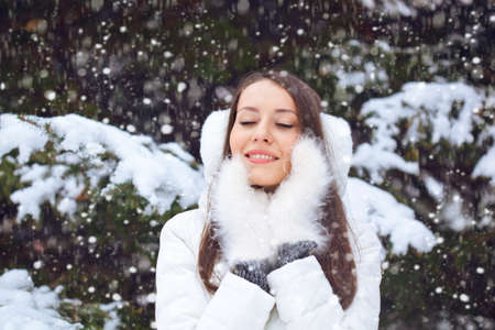 beautiful brunette woman standing under snowfall with closed eyesの写真素材
