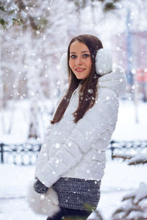 beautiful brunette woman standing in winter park under snowfallの写真素材