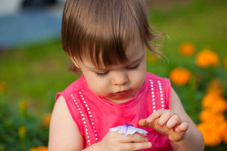 little girl wearing pink dress  holding flower outdoorsの写真素材