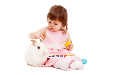 little girl painting easter eggs over white background, white rabbit sitting nearの写真素材
