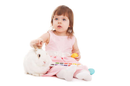 little girl painting easter eggs over white background, white rabbit sitting nearの写真素材