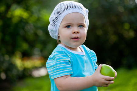 cute baby girl wearing blue dress walking in the park and holding green appleの写真素材