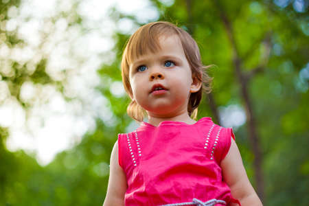 cute little girl in pink dress stading in park, low point of viewの写真素材