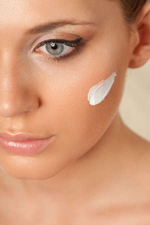 closeup beautiful woman face with cream on cheek over whiteの写真素材