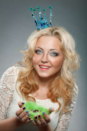 portrait of smiling woman wearing  blue princess crown and holding nest with quail eggsの写真素材