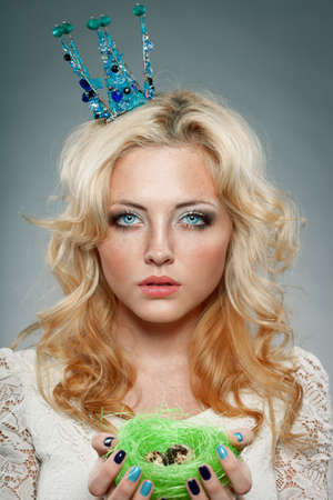 portrait of woman wearing  blue princess crown and holding nest with quail eggsの写真素材