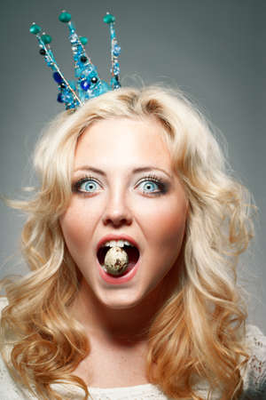 portrait of woman wearing  blue princess crown and holding quail egg in the mouthの写真素材