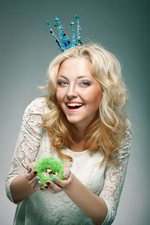 emotional portrait of woman wearing  blue princess crown and holding nest with quail eggsの写真素材