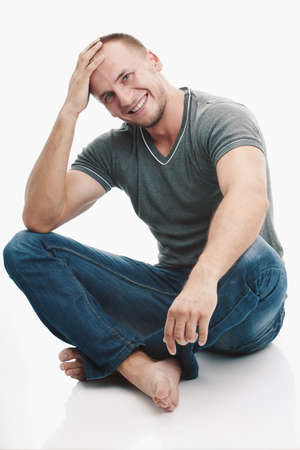 smiling strong casually dressed man over white background sitting on the floorの写真素材