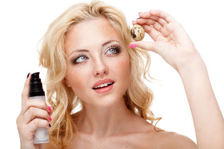 blonde woman with freckles on face holding quail egg and bottle of creamの写真素材