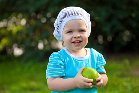 cute baby girl walking in the park and holding green appleの写真素材