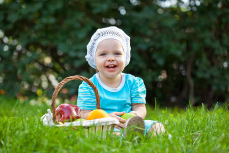 closeup portrait of baby girl sitting on the grass near basket with fruitsの写真素材