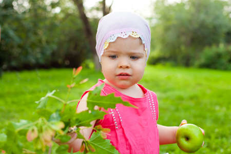 cute little girl walking in the park with green appleの写真素材