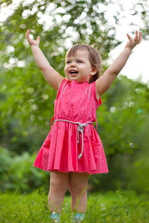 little girl stands on a meadow with raised handsの写真素材