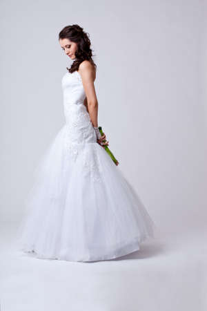 beautiful bride holding bouquet studio full length portrait, holding bouquet behind and looking downの写真素材