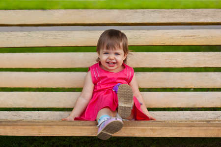 cute little girl sitting on bench in the parkの写真素材