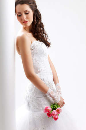 beautiful bride standing back to the  white column with closed eyes, studio shotの写真素材