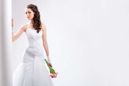 beautiful bride standing near white column, horizontal studio shotの写真素材