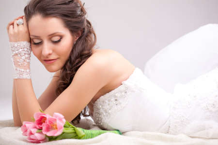 studio photograph of a bride posing on the floor and looking to the bouquetの写真素材
