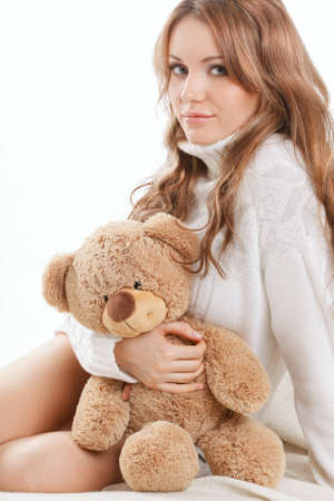 beautiful sexy woman wearing sweater sitting on the sofa and holding soft toyの写真素材
