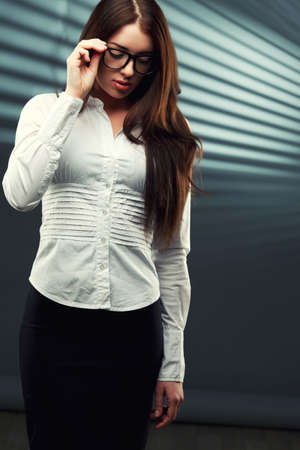 businesswoman wearing glasses in front of a striped background looking down and holding glassesの写真素材